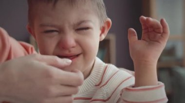 6 yaşında, Down sendromlu, evde ağlayan, şefkatli annesi tarafından teselli edilen beyaz bir çocuk.