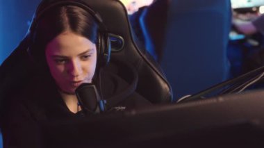 Geceleyin Esports Club 'da oynanan online birinci şahıs nişancı PC oyunu yarışması sırasında mikrofonla konuşan neşeli beyaz kız yavaşlıyor.