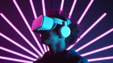 VR kulaklıklı Afrikalı Amerikalı oyuncu, arka planda mor ışıklı kılıçlarla karanlık odada dikilirken etrafına bakıyor.