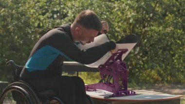 Güneşli bir günde, açık havada İngiliz anahtarıyla yatağını ayarlayan, dalış kıyafetli, orta boy beyaz bir adam.