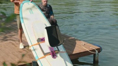 Profesyonel adaptif yemek sörfçüsü. Tekerlekli sandalyedeki dalgıç, ahşap iskelede beklerken suya uzanıyor.