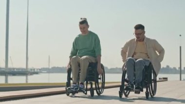 Güneşli bir günde tekerlekli sandalyeli iki genç beyaz adamın şehir seti boyunca yarışırkenki görüntülerini izliyoruz.