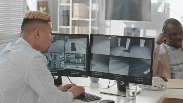与非洲裔美国人同事在现代办公室工作时 亚洲男性安全服务主管在电脑显示器上观看闭路电视摄像机的后视率有所下降 — 图库视频影像