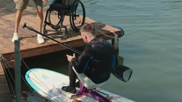 화창한 적응형 Supboard에 앉아있는 잠수복 패들링에 장애가있는 코카서스 사람의 샷에서 — 비디오