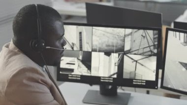 Ofisteki bilgisayar monitöründe birden fazla kapalı devre güvenlik kamerasını izleyen ciddi siyahi erkek güvenlik müdürü yavaşlıyor.
