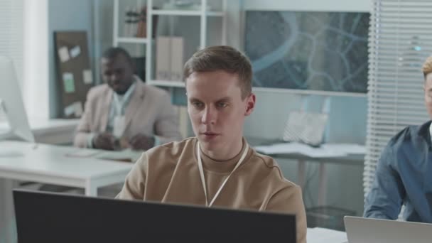 若い濃縮された白人男性データエンジニアのチェストアップスローモーションは デスクトップコンピュータ上の情報を監視しながら 同僚の多様なチームと一緒にセキュリティ機関で働いています — ストック動画