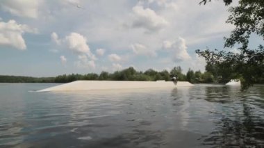 Engelli profesyonel wakeboardcunun geniş açılı görüntüsü uyarlanabilir uyanma tahtasına oturması ve açık havada suda dans ederken kayarak kayması.