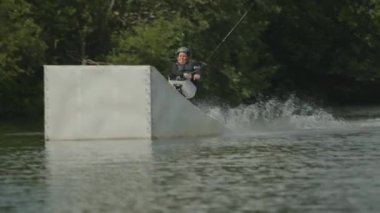 Güneşli bir günde, bacakları olmayan beyaz bir çocuk açık havada uysal bir wakeboard çalışması yapıyor.