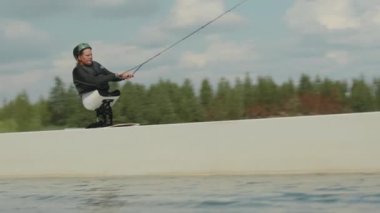 Engelli genç wakeboardcu sürgülü kaydırak kullanarak suyun içinde uyarlanabilir açık havada sörf yapıyor.