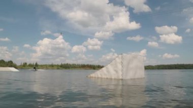 Engelli genç sörfçülerin yavaş yavaş nehir kenarından ip tutarak atlarken yaz mevsiminde uyanış sörfü becerileri geliştirmesi.