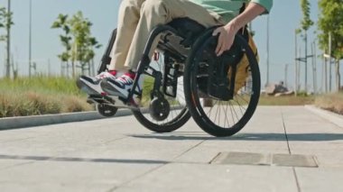 Özürlü genç beyaz adamın portresi. Yazın tekerlekli sandalyesiyle dışarıda oyun oynarken kameraya bakıyor.
