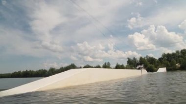Bacaksız genç sörfçülerin yavaşlaması, uyarlanabilir wakeboard çalışması yapıyor, kaydırağın üzerinden ip tutarak atlayarak numaralar yapıyor.