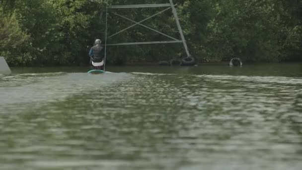 川沿いのロープで引っ張られている適応覚醒ボードに座っている障害のある男性サーファーのバックビュー — ストック動画