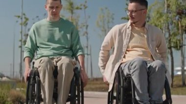 Yazın kaldırım boyunca tekerlekli sandalyeyle gezen iki beyaz erkek arkadaşı yukarı kaldır.