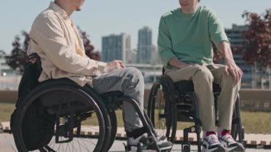 Tekerlekli sandalyedeki iki beyaz arkadaşın yaz yürüyüşü sırasında şehir setinde sohbet ederken çekilen pozu.