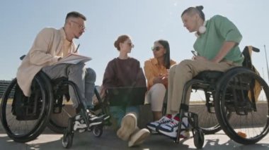 Dolly, güneşli bir günde şehir setinde oturup iş tartışan tekerlekli sandalyedeki iki genç beyaz adamı ve iki genç kadını vuruyor.