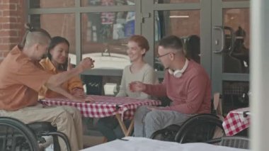 Kentteki açık yaz kafeteryasında öğle yemeği yedikten sonra iki beyaz erkek ve bayan arkadaşlarının birbirleriyle vedalaştıkları orta boy bir fotoğraf.