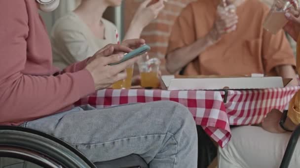 夏天的一天 坐在户外咖啡馆里与朋友们一起围坐在桌旁 一个无法辨认的坐在轮椅上的男人在智能手机上浏览的照片被剪下来了 — 图库视频影像