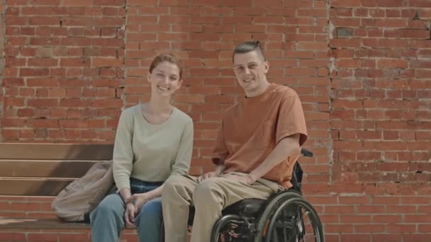 年轻白种人快乐的轮椅男与漂亮的女友在户外的红砖墙前摆姿势拍照 这是他的肖像 — 图库视频影像