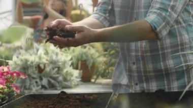 Kareli gömlekli ve hasır şapkalı beyaz bir adam elleriyle toprağı gevşetiyor ve kızıyla birlikte bitki yetiştirme odasında çalışıyor.