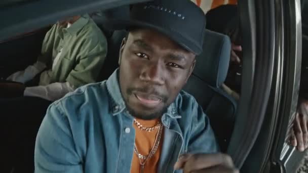 穿着斜纹棉布衬衫 头戴帽子 脚镣的黑人坐在他的旧校车的司机座位上 同伴们一起听嘻哈音乐 — 图库视频影像
