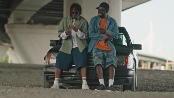 两名非洲裔美国人靠着停放在桥下的旧校车的引擎盖 一边听着嘻哈音乐一边跳舞 — 图库视频影像