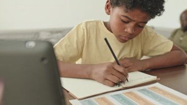 Modern oturma odasındaki masada oturup okul ödevlerini yaparken kitap yazan Afro-Amerikan çocuk sandığı.
