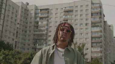 Afrika kökenli Amerikalı bir adamın gündüz vakti kameraya rap yaptığı orta boy bir fotoğraf.