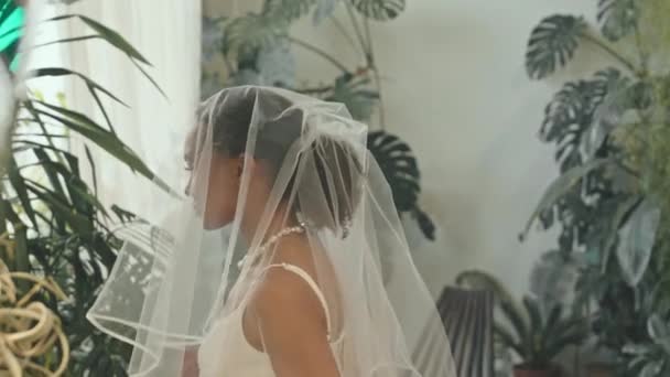 在室内举行的婚礼上 身穿雅致的黑色西装的快乐的非洲裔新郎站起来 与美丽的新娘相遇 摘下面纱 面带微笑 温柔地拥抱对方 — 图库视频影像