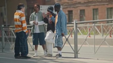 Üç Afro-Amerikalı ve beyaz erkek arkadaşlarının gündüz vakti sokakta sigara içerken ve sohbet ederken tam boy çekimleri.