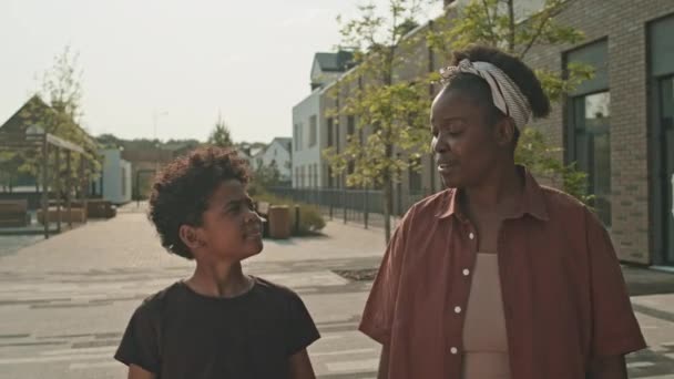 アフリカ系アメリカ人の若い女性と12歳の息子が夏に屋外を散歩しながらチャットするのを待つ — ストック動画