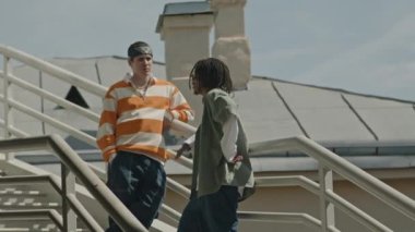Güneşli bir günde, iki farklı hipster arkadaşın açık havada, merdivenlerden çatıya çıkıp sohbet etmelerinin orta boy görüntüsü.
