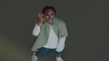 Genç siyah gözlüklü hippi gündüz vakti rap yaparken kafasını kaldırıyor.