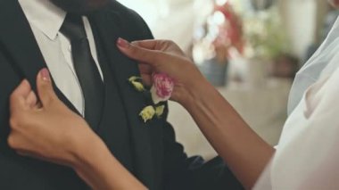 Tanımlanamayan gelinin, damat elbisesinin cebindeki gül yaka çiçeğini düzeltirken düğün töreninden önce son hazırlıklarını yaparken çekilmiş bir fotoğrafı.