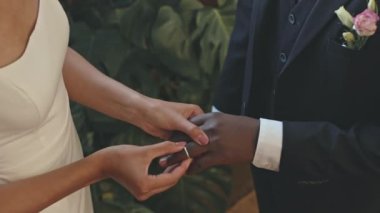 Tanımlanamayan gelinin, düğün sırasında arka planda yeşil tropik yapraklarla sevgili damadının parmağına yüzük taktığı kesikli fotoğraf.