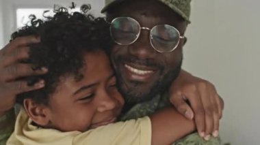 Ordudan döndükten sonra küçük oğlunu kucaklayan, kamuflaj üniformalı zenci askerin orta boy yakın çekimi.