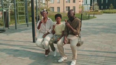 Mutlu Afro-Amerikan ailesi, sıcak yaz günlerinde evlerinin önünde salıncakta sallanırken sohbet edip dondurma yiyorlar.