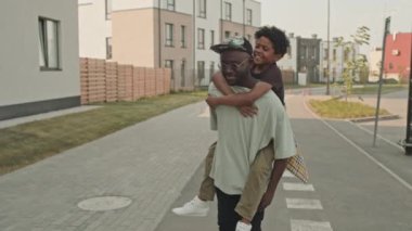 Güneşli bir günde açık havada birlikte vakit geçirirken babalarının sırtında gezen neşeli Afrikalı Amerikalı çocuğun orta boy fotoğrafı.