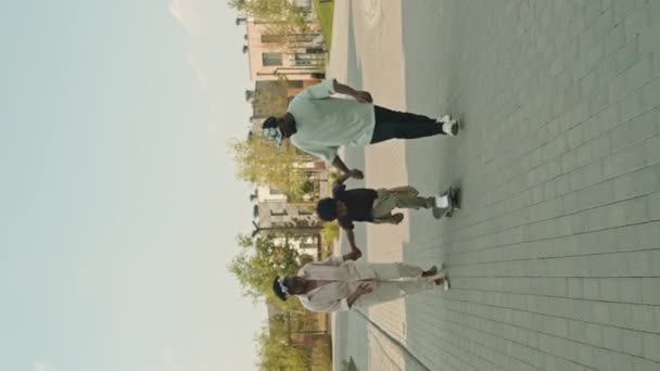 歩道でスケートボードに乗っているアフリカ系アメリカ人の男の子と彼の両親が彼を助け 夏に屋外で余暇を過ごした — ストック動画