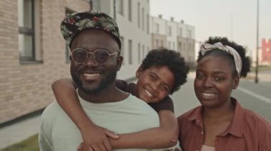 Güneşli bir günde şehrin dışında kameraya gülümseyen modern siyah aile portresi