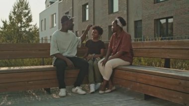 Günümüz Afro-Amerikan ailesi. Oğulları küçük yaşta tahta bankta, gün ışığında birlikte oturuyorlar. Boş zamanlarını dışarıda geçiriyorlar.
