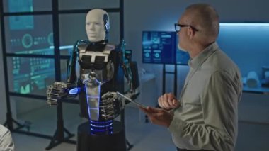 İnsanımsı robotu laboratuvarda etkinleştirirken orta büyüklükte beyaz erkek mühendisin dijital tablet kullanırken görüntüsü.