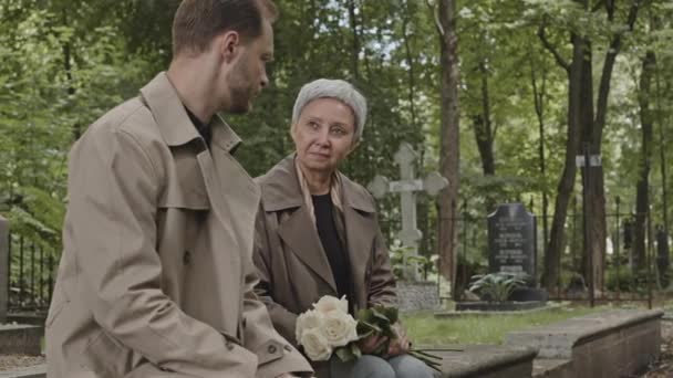 Medium Shot Mother Adult Son Sitting Gravestone Cemetery Having Conversation — Stock Video