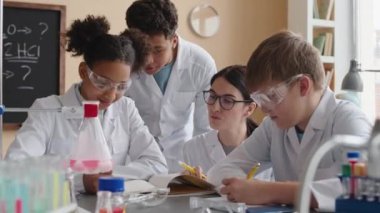Genç bayan kimya öğretmeninin belini kaldırın. Çok ırklı bir grup liseli öğrenciye ders verin. Laboratuvardaki cam şişede kimyasal reaksiyon gözlemleyin.