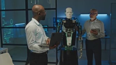İki erkek robotik mühendisinin bilim laboratuarında birlikte çalışırken insansı robotun etkinleştirilmesini tartışırken orta boy görüntüleri.