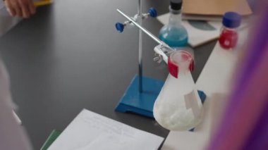 Laboratuvar önlüğüyle tanınmayan öğrencinin, cam şişeye tanımlanamayan sarı sıvıyı dökerek kuru buzu buharlaştırması ve okul laboratuarında kimyasal deney yapması.