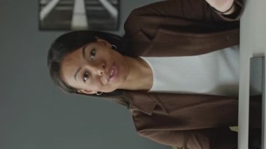 Minimalist ofisteki beyaz ofis masasında oturan, kameraya konuşan genç, çift ırklı kadının dik bel görüntüsü.