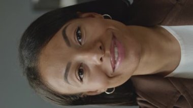 Minimalist ofiste kameraya konuşan çekici, çift ırklı genç kadının dikey görüntüsü.