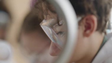 Bilim okulu laboratuarında bilimsel araştırma yapan kıvırcık saçlı liseli çocuğun orta ölçekli büyüteç fotoğrafı sayesinde.