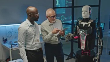 İki farklı erkek robotik mühendisinin dijital tablette robot gibi insanları kontrol ederken laboratuvarda çalışırken orta boy görüntüsü.
